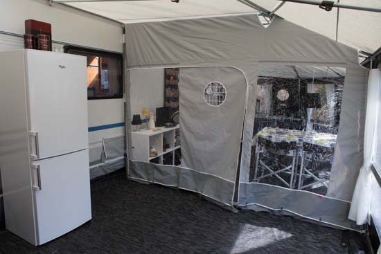 Så er skillevæggen kommet op. Den gøres fast midt i teltet i loftet, til fronten og ind til campingvognen. Alle stænger og profiler følger med. Desværre kunne vi ikke pløkke den gennem gulvet, så græskanten blev holdt nede af sten.