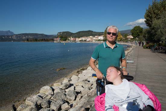 Søpromenaden med bænke og oliventræer. I baggrunden ses Bardolino. Sissel er ikke helt glad for det skarpe sollys, hvilket måske fremgår af billedet